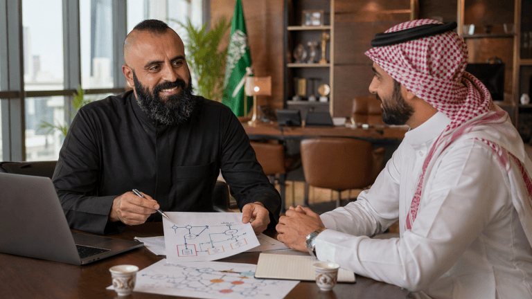 AI-generated illustration of Waseem Sendi sketching a workflow beside a laptop while discussing it with another person.