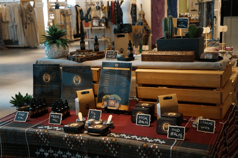 An early Diggn’It market display in Jeddah, with beard-care bottles, tins, wooden crates, handwritten labels and a traditional patterned cloth.