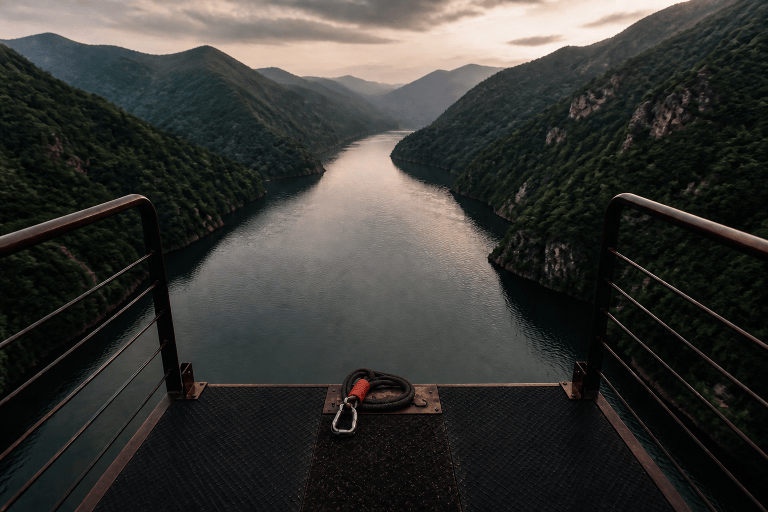 A symbolic view from an empty bungee-jumping platform above a wide river between green mountains.